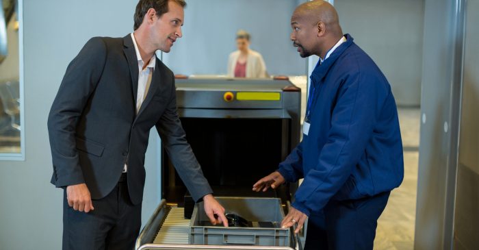 Airport security officer interacting with commuter while checking a package in airport terminal